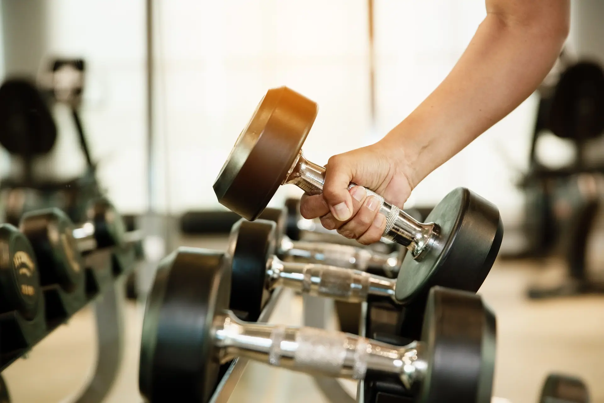 A hand picking up a dumbbell from a rack.