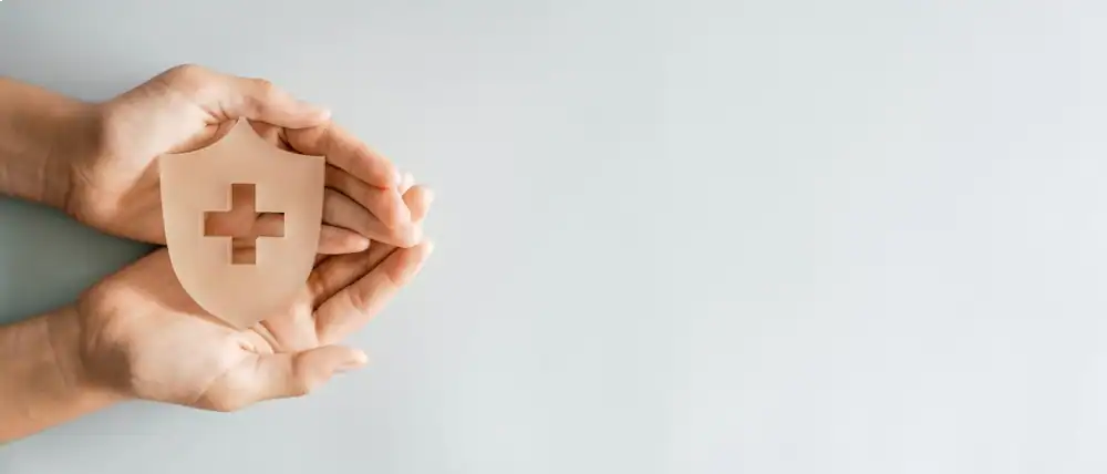 Hands holding a shield with a medical cross symbol for health protection.