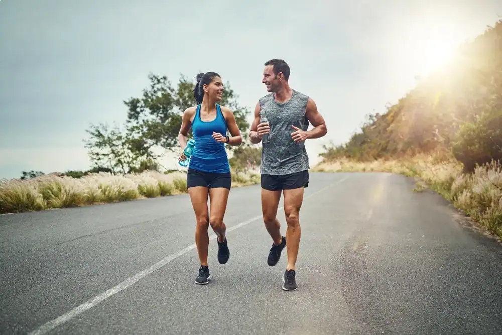Healthy couple jogging outdoors on a scenic road at sunrise.